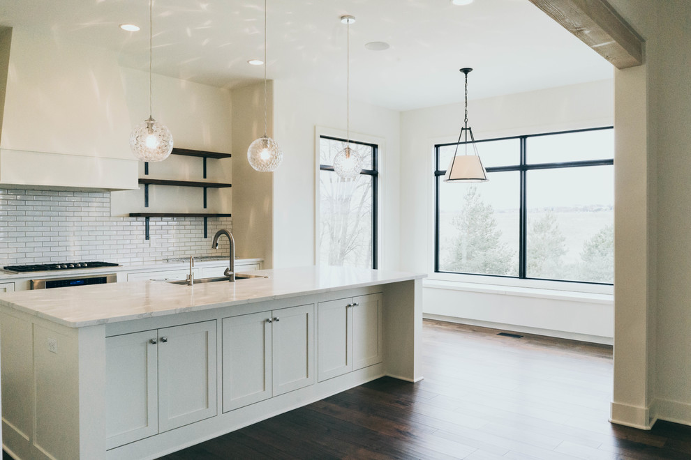 Example of an enclosed kitchen design in Omaha with a farmhouse sink, shaker cabinets, white cabinets, quartz countertops, stainless steel appliances and an island