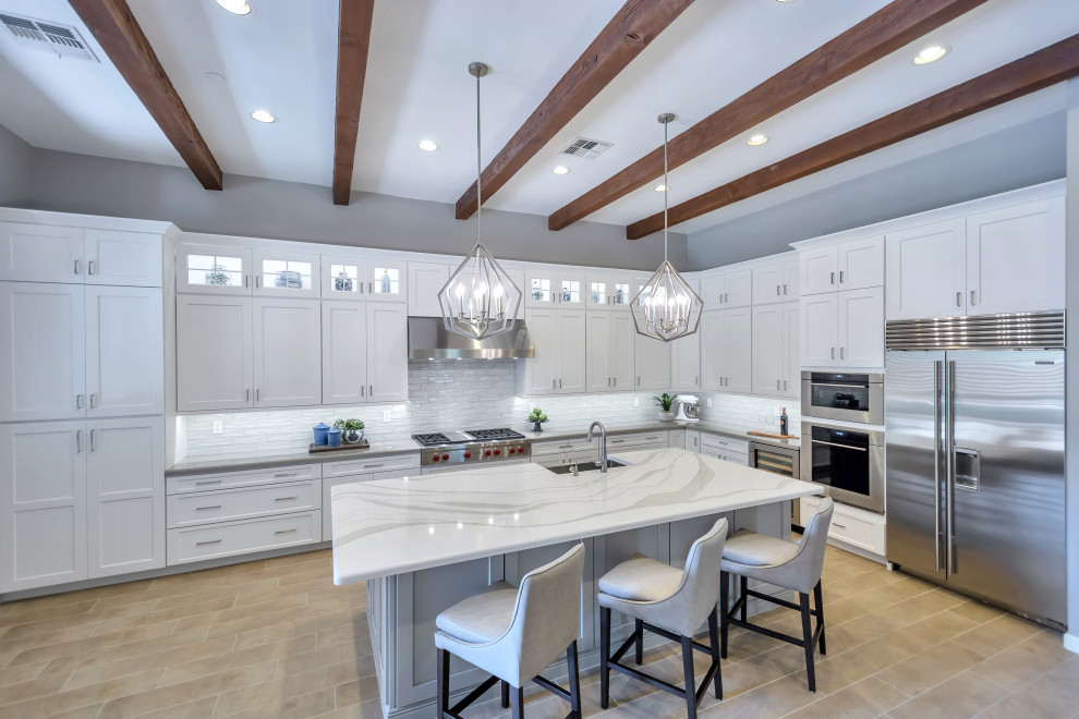 Inspiration for a large transitional l-shaped porcelain tile and brown floor eat-in kitchen remodel in Phoenix with a farmhouse sink, shaker cabinets, white cabinets, quartz countertops, white backsplash, subway tile backsplash, stainless steel appliances, an island and gray countertops