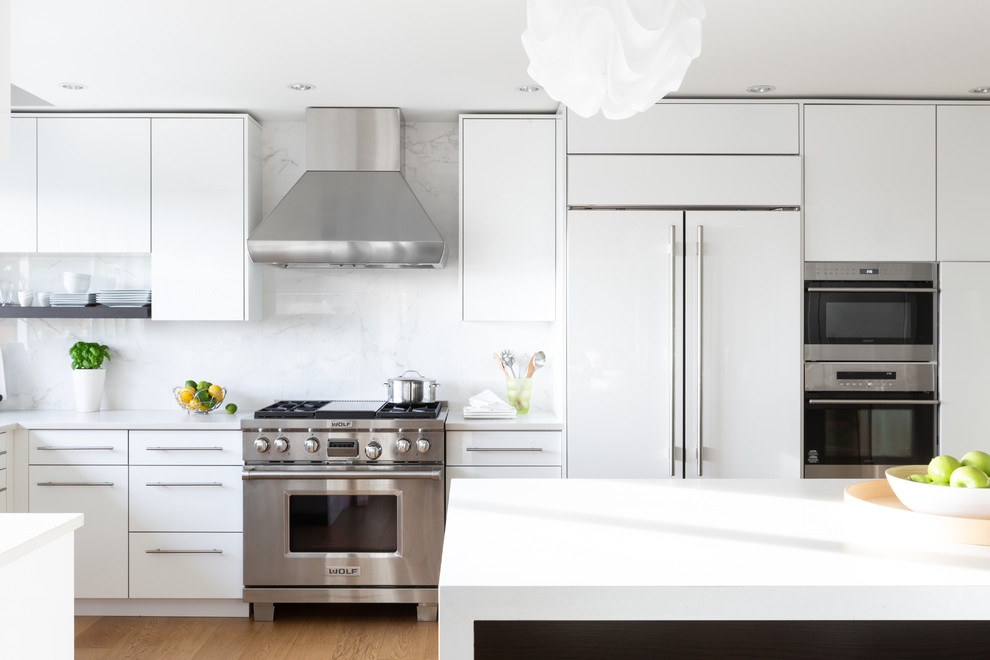 Design ideas for a mid-sized modern l-shaped eat-in kitchen in Vancouver with an undermount sink, flat-panel cabinets, white cabinets, white splashback, marble splashback, stainless steel appliances, light hardwood floors, with island, brown floor and white benchtop.