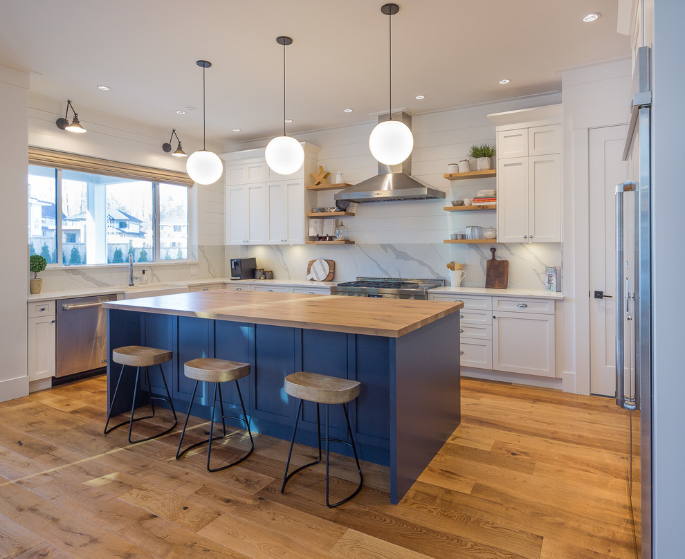 Photo of a transitional u-shaped kitchen in Vancouver with a farmhouse sink, shaker cabinets, white cabinets, wood benchtops, stainless steel appliances, medium hardwood floors, with island, brown floor and brown benchtop.