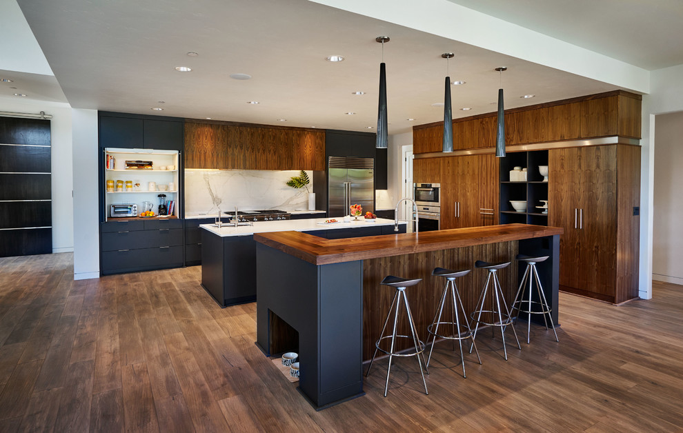 Inspiration for an expansive contemporary l-shaped eat-in kitchen in Portland with flat-panel cabinets, medium wood cabinets, white splashback, multiple islands, an undermount sink, quartz benchtops, stainless steel appliances, medium hardwood floors and stone slab splashback.