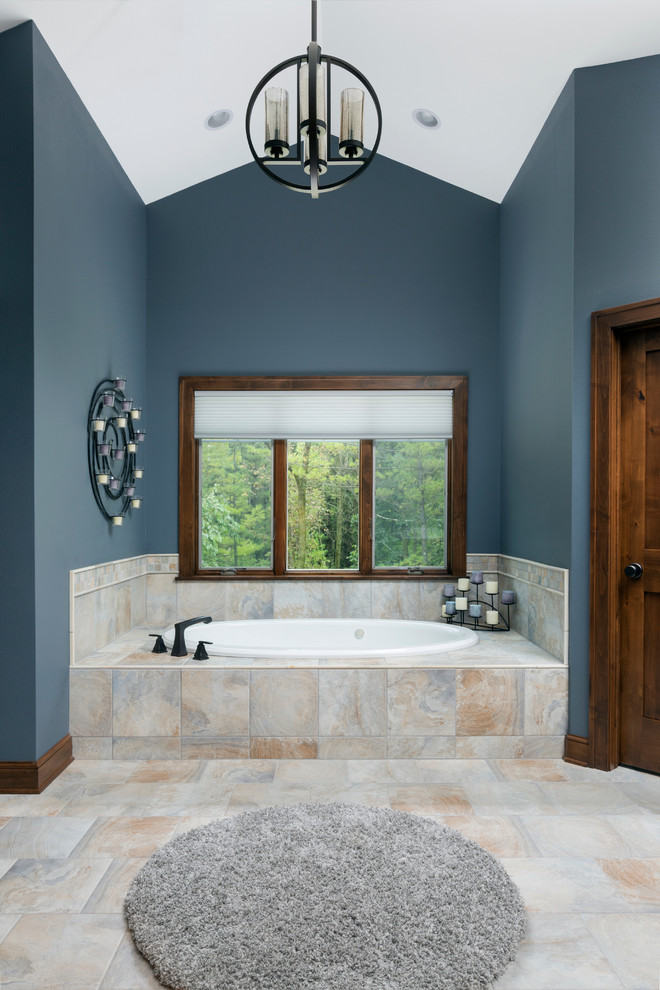 Photo of a large traditional master bathroom in Milwaukee with a hot tub, beige tile, porcelain tile, blue walls, porcelain floors, a drop-in sink, marble benchtops, flat-panel cabinets, brown cabinets, a curbless shower, beige floor, a hinged shower door and beige benchtops.