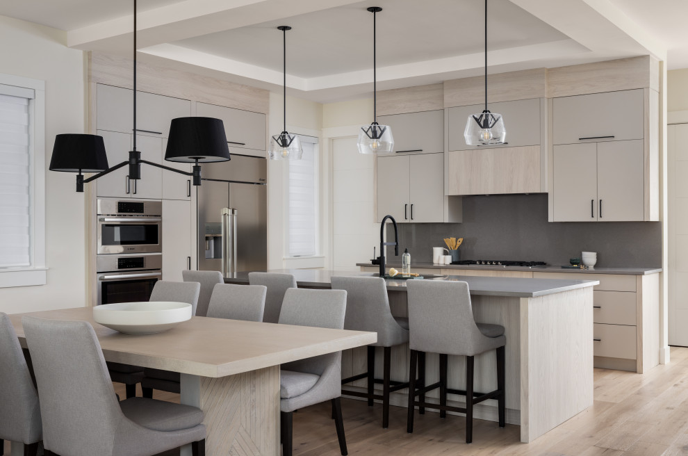 Inspiration for a mid-sized modern l-shaped eat-in kitchen in Calgary with a double-bowl sink, flat-panel cabinets, light wood cabinets, quartz benchtops, grey splashback, engineered quartz splashback, stainless steel appliances, light hardwood floors, with island, beige floor, grey benchtop and coffered.