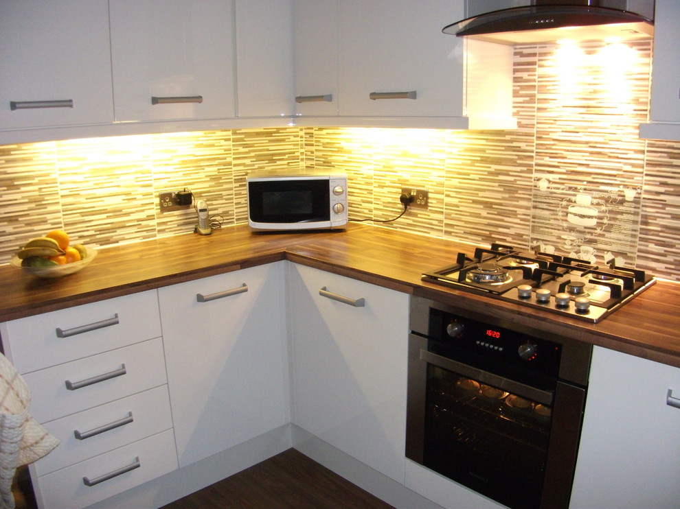Medium sized modern l-shaped enclosed kitchen with a single-bowl sink, flat-panel cabinets, white cabinets, laminate countertops, multi-coloured splashback, ceramic splashback, stainless steel appliances and dark hardwood flooring.