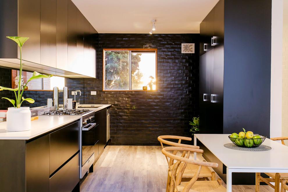 Inspiration for a beach style galley eat-in kitchen in Adelaide with an undermount sink, flat-panel cabinets, black cabinets, metallic splashback, mirror splashback, black appliances, light hardwood floors, no island, beige floor and white benchtop.