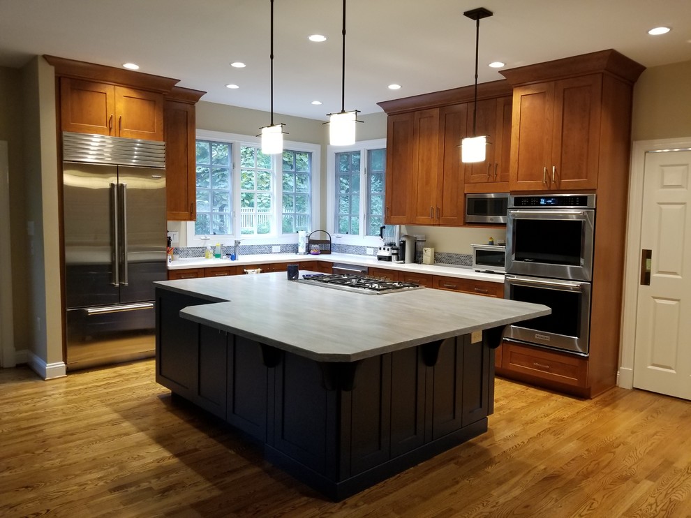 Inspiration for a mid-sized transitional l-shaped eat-in kitchen in DC Metro with an integrated sink, recessed-panel cabinets, medium wood cabinets, solid surface benchtops, blue splashback, mosaic tile splashback, stainless steel appliances, medium hardwood floors, a peninsula, brown floor and blue benchtop.