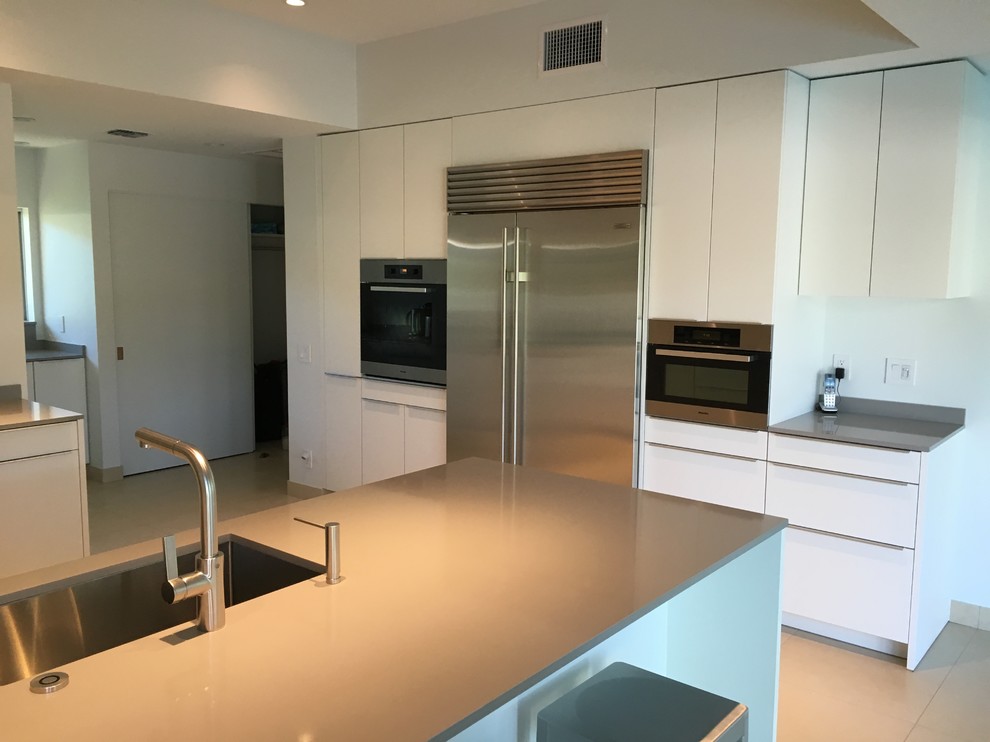 This is an example of a mid-sized contemporary u-shaped kitchen in Hawaii with a single-bowl sink, flat-panel cabinets, white cabinets, quartz benchtops, stainless steel appliances and a peninsula.