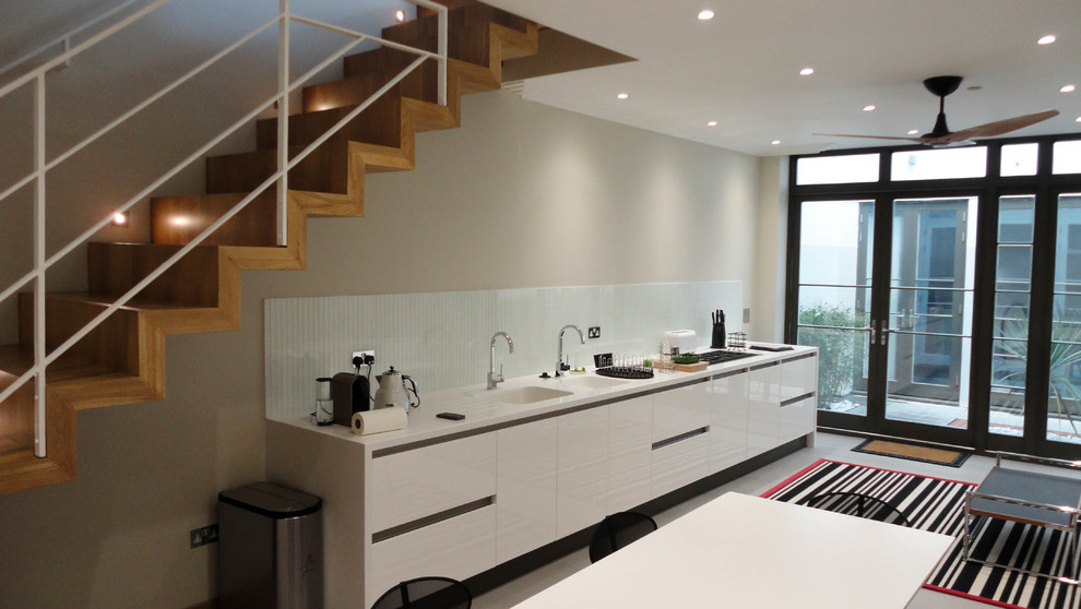 Large contemporary single-wall eat-in kitchen in London with limestone floors, an integrated sink, flat-panel cabinets, white cabinets, solid surface benchtops, white splashback, porcelain splashback, stainless steel appliances and no island.