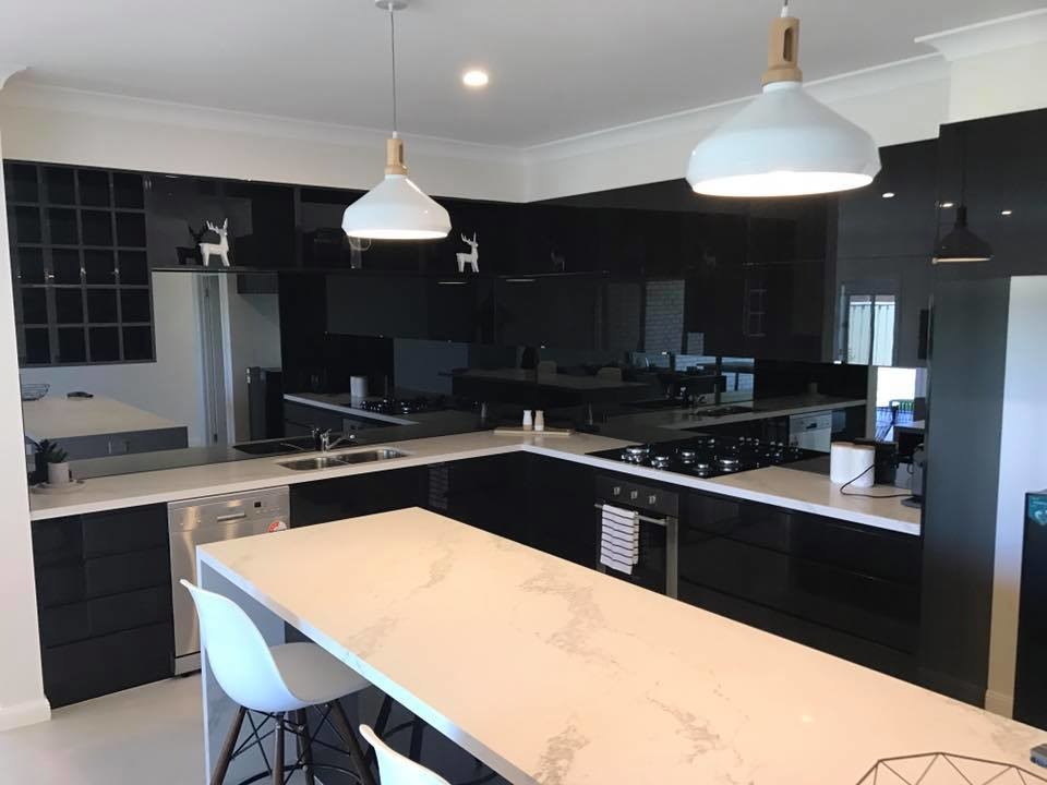 This is an example of a large modern l-shaped open plan kitchen in Adelaide with quartzite benchtops, black splashback, glass tile splashback, black appliances and with island.