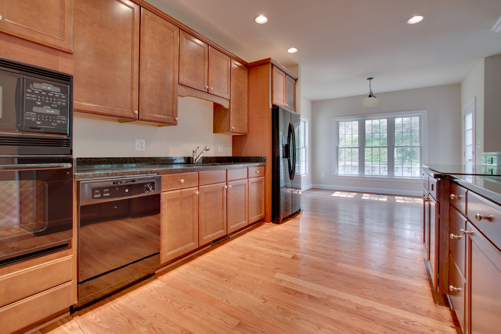 Inspiration for a galley light wood floor open concept kitchen remodel in DC Metro with recessed-panel cabinets, medium tone wood cabinets, granite countertops, black appliances, an island and an undermount sink
