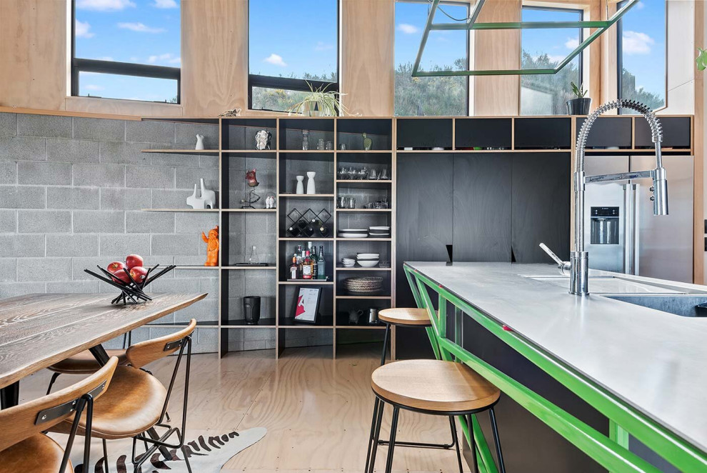 Inspiration for a mid-sized industrial galley kitchen pantry in Wellington with an integrated sink, recessed-panel cabinets, black cabinets, stainless steel benchtops, black splashback, ceramic splashback, stainless steel appliances, plywood floors, with island and timber.
