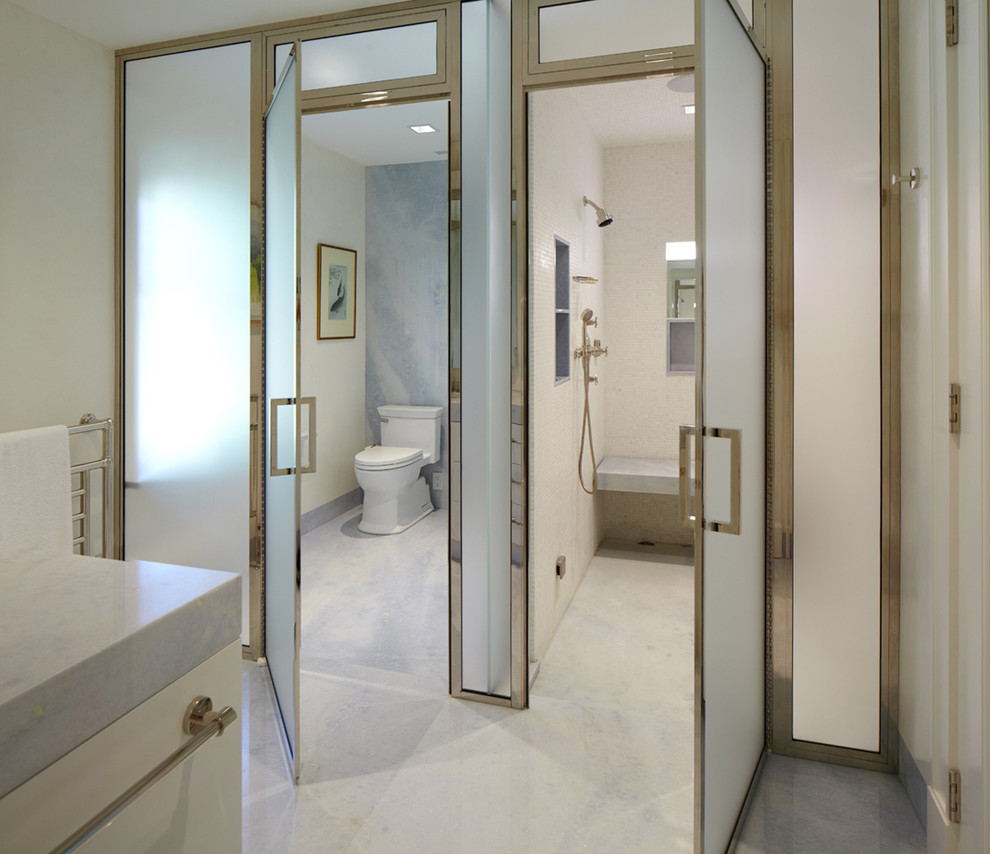 This is an example of an expansive transitional master bathroom in New York with flat-panel cabinets, white cabinets, an alcove shower, white walls, marble benchtops, a two-piece toilet, white tile, marble floors, stone slab, a hinged shower door, grey floor and an enclosed toilet.