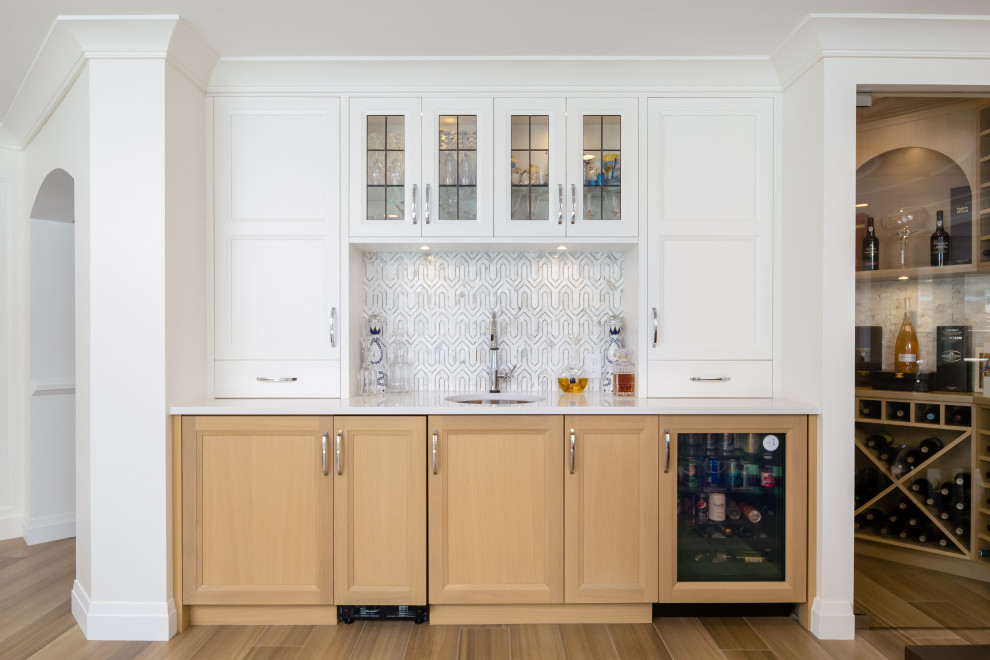 Photo of a traditional single-wall wet bar in Vancouver with a submerged sink, recessed-panel cabinets, medium wood cabinets, marble splashback, medium hardwood flooring and brown floors.