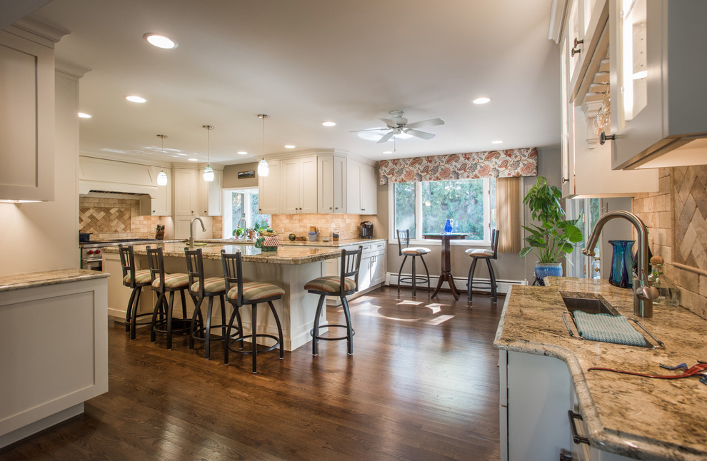 Large transitional u-shaped medium tone wood floor and brown floor eat-in kitchen photo with an undermount sink, shaker cabinets, white cabinets, granite countertops, beige backsplash, travertine backsplash, paneled appliances and an island