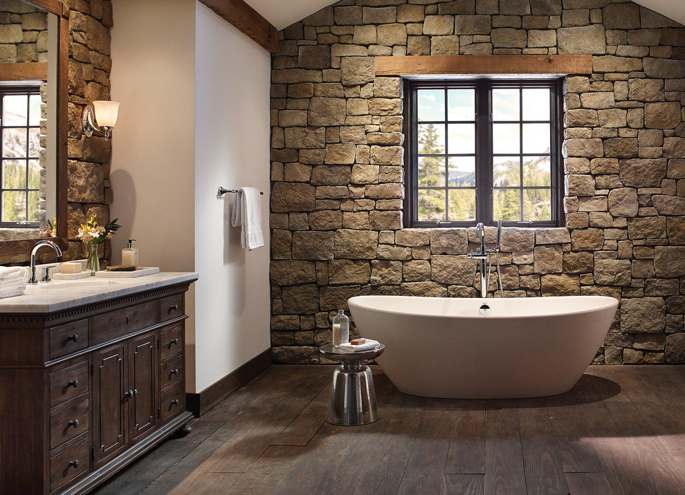 Inspiration for a mid-sized country master bathroom in Raleigh with dark wood cabinets, a freestanding tub, multi-coloured walls, dark hardwood floors, an undermount sink, beige tile, brown tile, stone tile, engineered quartz benchtops and flat-panel cabinets.