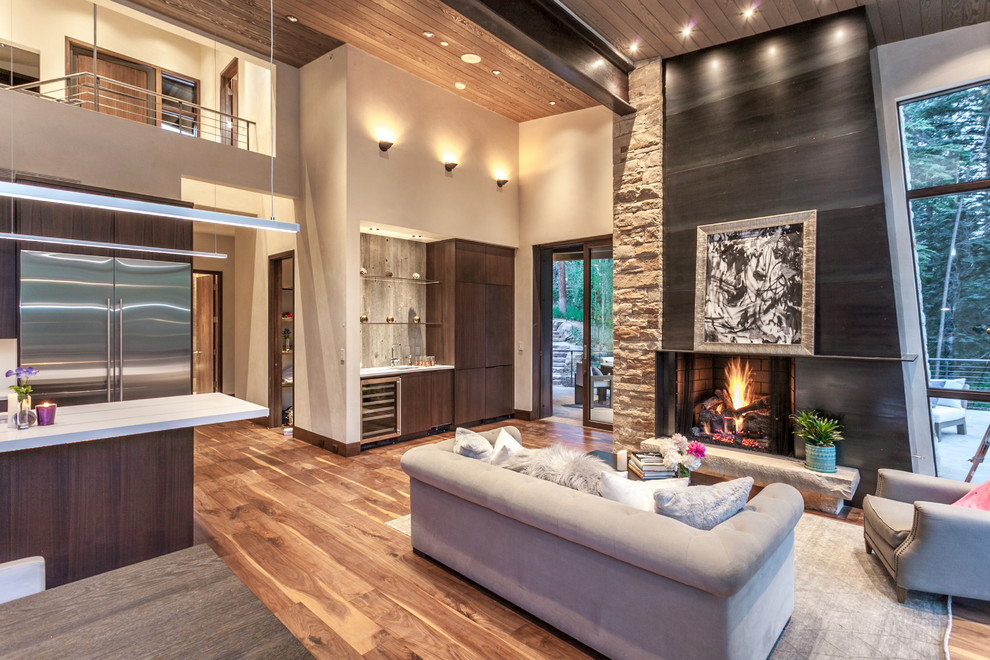 Large country open concept living room in Denver with a home bar, medium hardwood floors, a standard fireplace, a metal fireplace surround, brown floor and beige walls.