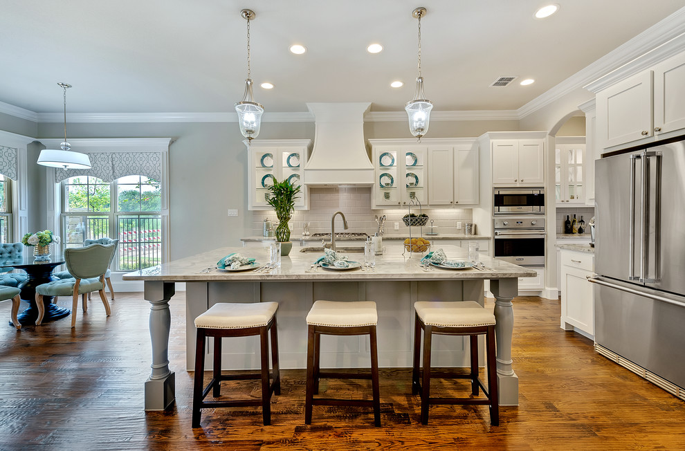 This is an example of a transitional open plan kitchen in Dallas with white cabinets, white splashback, subway tile splashback, stainless steel appliances and with island.