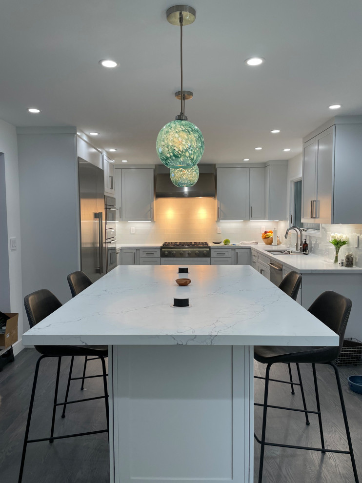 Inspiration for a large contemporary u-shaped kitchen/diner in San Francisco with a double-bowl sink, shaker cabinets, white cabinets, engineered stone countertops, glass tiled splashback, stainless steel appliances, dark hardwood flooring, an island, grey floors and white worktops.