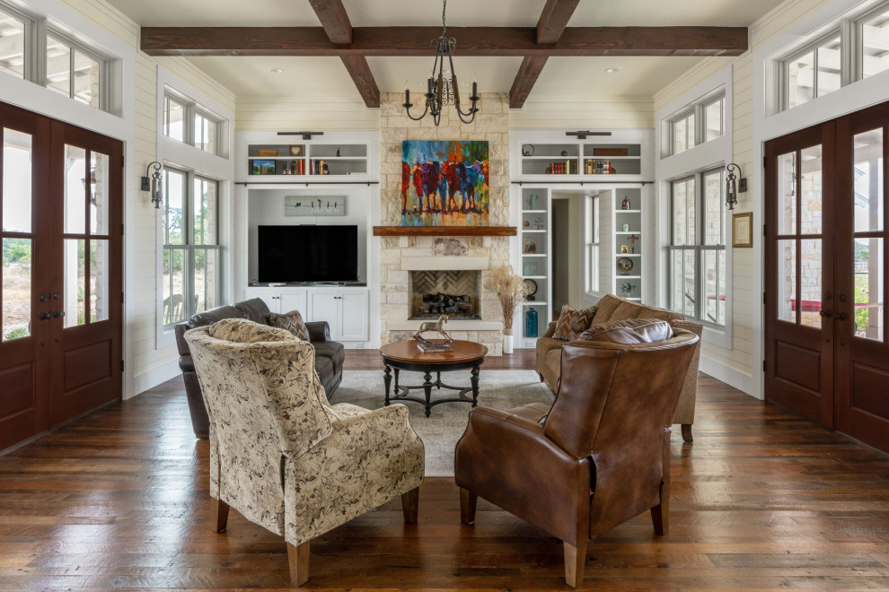 Photo of a large country open concept living room in Austin with a library, beige walls, dark hardwood floors, a standard fireplace, a stone fireplace surround, brown floor, exposed beam and planked wall panelling.