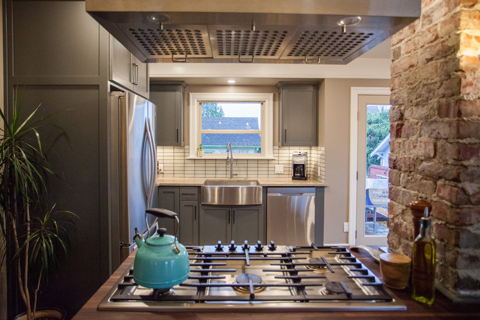 Open concept kitchen - small transitional l-shaped dark wood floor and brown floor open concept kitchen idea in Seattle with a farmhouse sink, shaker cabinets, gray cabinets, stainless steel appliances, an island, granite countertops, white backsplash, porcelain backsplash and beige countertops
