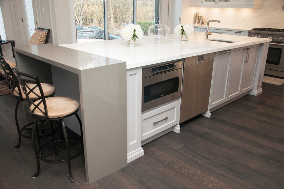 Example of a large transitional l-shaped dark wood floor and brown floor enclosed kitchen design in Toronto with an undermount sink, shaker cabinets, white cabinets, quartz countertops, white backsplash, marble backsplash, stainless steel appliances, an island and white countertops
