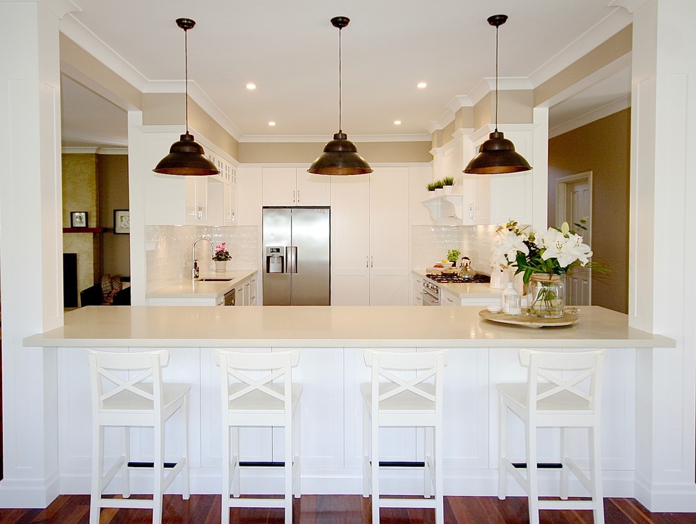 This is an example of a mid-sized transitional u-shaped kitchen in Sydney with a drop-in sink, shaker cabinets, dark wood cabinets, quartz benchtops, white splashback, ceramic splashback, stainless steel appliances, dark hardwood floors, with island and brown floor.