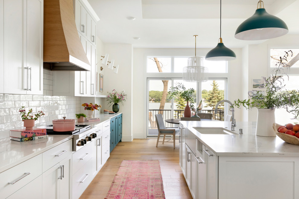 Kitchen - large coastal l-shaped light wood floor and coffered ceiling kitchen idea in Minneapolis with an undermount sink, flat-panel cabinets, white cabinets, quartz countertops, white backsplash, ceramic backsplash, stainless steel appliances, an island and gray countertops