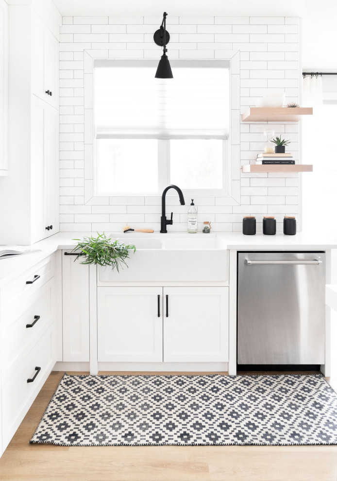 Design ideas for a mid-sized scandinavian l-shaped eat-in kitchen in Calgary with a farmhouse sink, shaker cabinets, white cabinets, quartz benchtops, white splashback, porcelain splashback, stainless steel appliances, with island, beige floor and white benchtop.