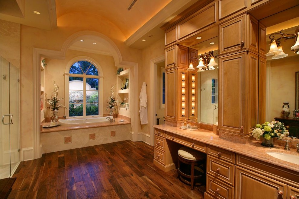 This is an example of a mediterranean master bathroom in Miami with a drop-in tub, raised-panel cabinets, granite benchtops, dark hardwood floors and medium wood cabinets.