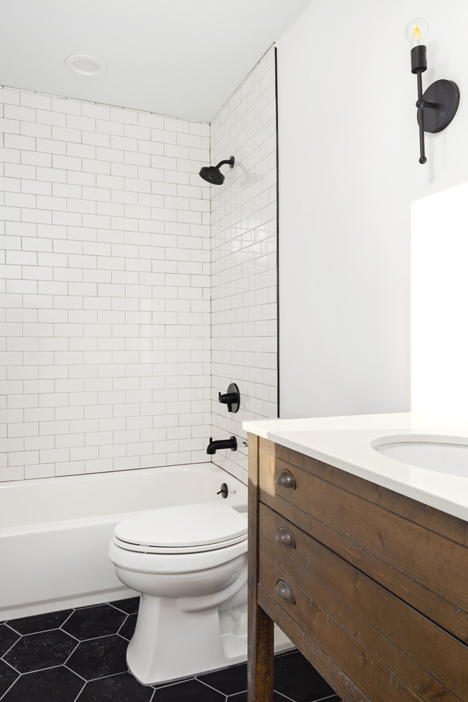 Design ideas for a mid-sized country kids bathroom in Denver with furniture-like cabinets, distressed cabinets, a shower/bathtub combo, a two-piece toilet, white tile, ceramic tile, white walls, ceramic floors, an undermount sink, marble benchtops, black floor and beige benchtops.