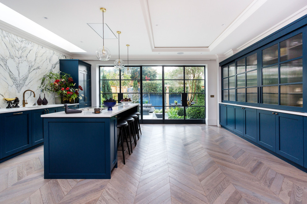 Große Moderne Küche mit Schrankfronten im Shaker-Stil, blauen Schränken, Quarzit-Arbeitsplatte, Küchenrückwand in Weiß, Rückwand aus Marmor, schwarzen Elektrogeräten, Kücheninsel, braunem Boden und weißer Arbeitsplatte in London