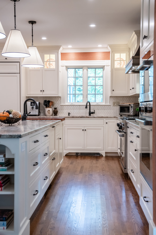 Inspiration for a mid-sized traditional l-shaped separate kitchen in Portland Maine with an undermount sink, recessed-panel cabinets, white cabinets, granite benchtops, white splashback, panelled appliances, medium hardwood floors, with island, brown floor and beige benchtop.