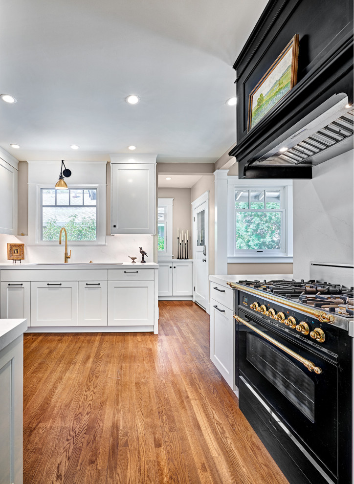 This is an example of a small arts and crafts u-shaped eat-in kitchen in Sacramento with an undermount sink, shaker cabinets, black cabinets, quartz benchtops, white splashback, engineered quartz splashback, panelled appliances, medium hardwood floors, no island, multi-coloured floor and white benchtop.
