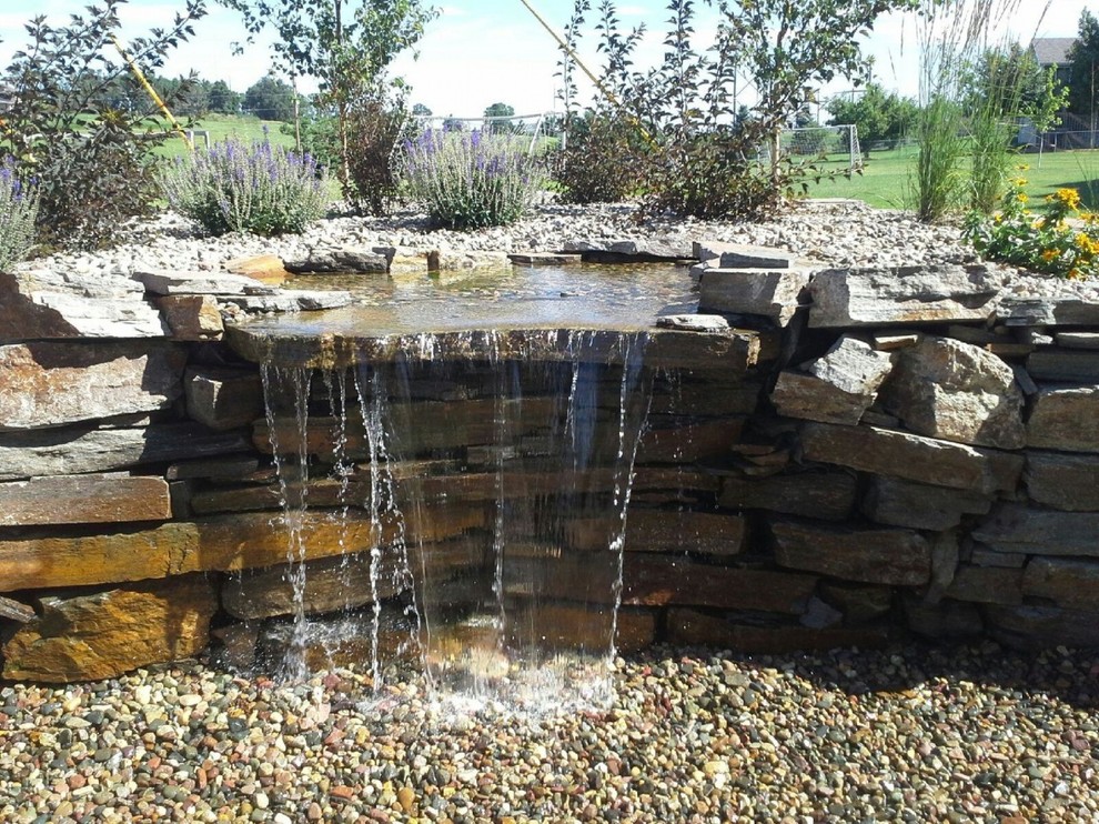 This is an example of a rustic full sun backyard mulch water fountain landscape for summer.