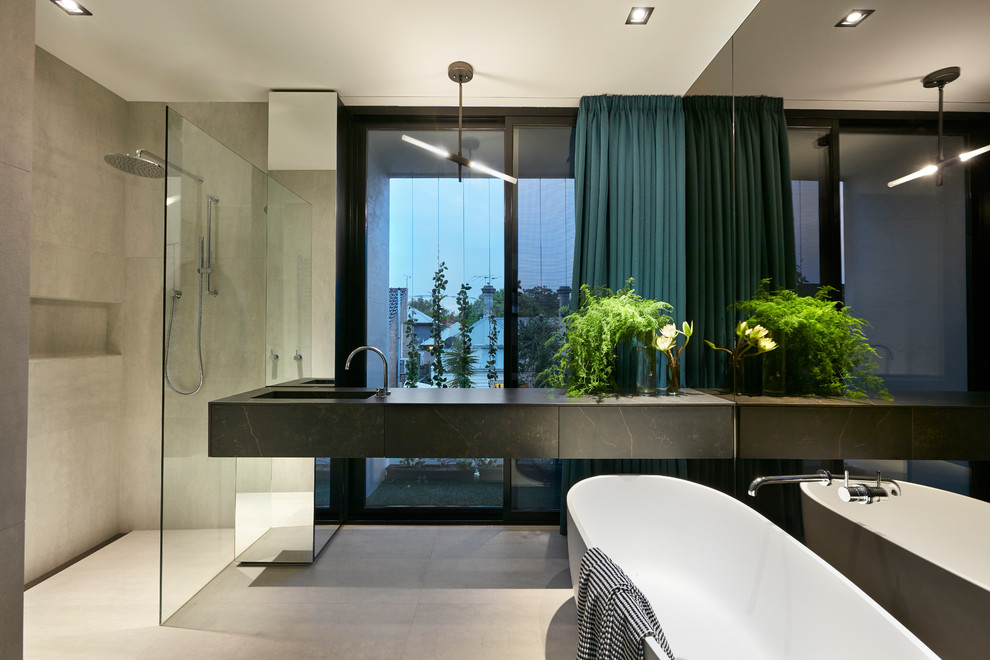 Design ideas for a large contemporary master bathroom in Melbourne with black cabinets, a freestanding tub, an open shower, a wall-mount toilet, gray tile, porcelain tile, grey walls, porcelain floors, an integrated sink, engineered quartz benchtops, grey floor, an open shower, black benchtops and flat-panel cabinets.