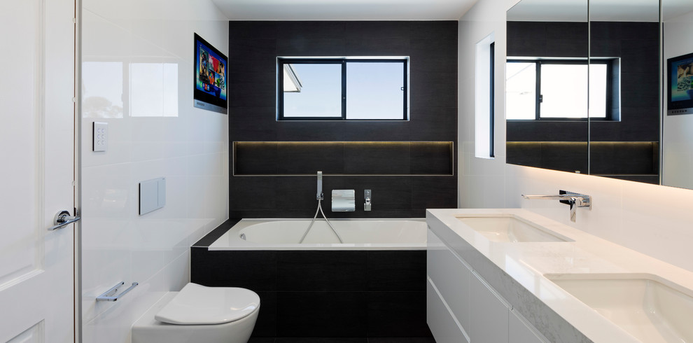 This is an example of a large contemporary master bathroom in Sydney with beaded inset cabinets, white cabinets, a hot tub, an alcove shower, a wall-mount toilet, black and white tile, porcelain tile, white walls, ceramic floors, an undermount sink, engineered quartz benchtops, black floor, a sliding shower screen, white benchtops, a niche, a double vanity and a floating vanity.