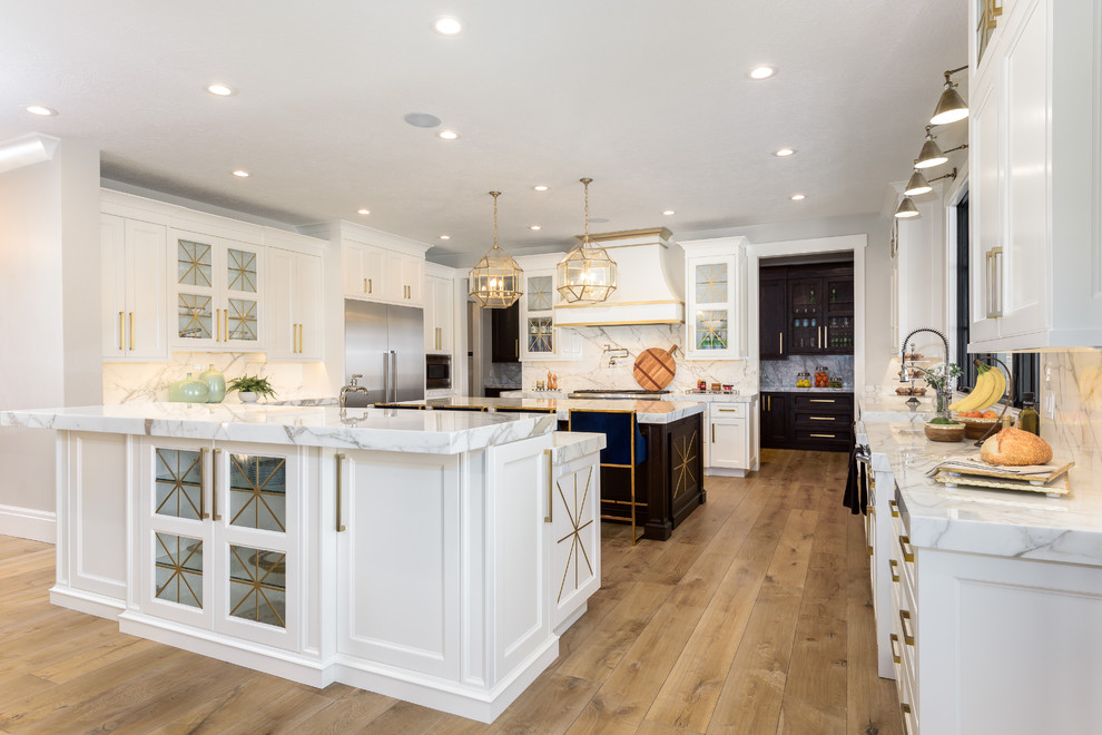 This is an example of a large transitional single-wall separate kitchen in Salt Lake City with white cabinets, grey splashback, medium hardwood floors, brown floor, grey benchtop, a farmhouse sink, shaker cabinets, marble benchtops, marble splashback, stainless steel appliances and multiple islands.