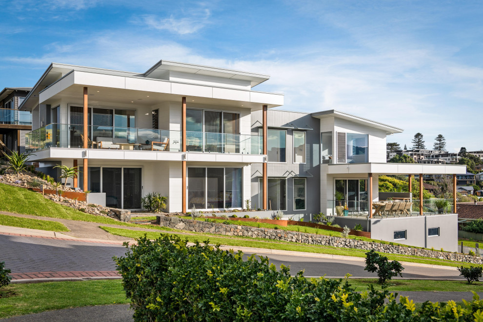 Photo of an expansive beach style split-level beige house exterior in Wollongong with mixed siding, a flat roof and a metal roof.