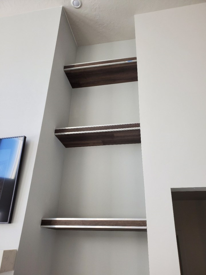Imagen de sala de estar abovedada minimalista grande con suelo laminado, marco de chimenea de yeso y televisor retractable