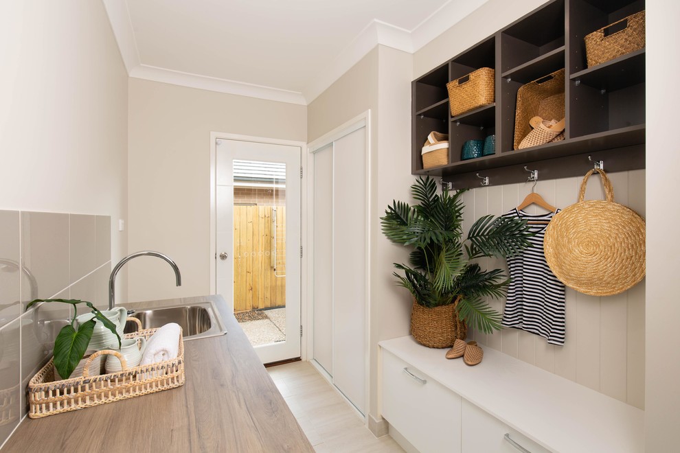 Beach style galley dedicated laundry room in Brisbane with a drop-in sink, flat-panel cabinets, white cabinets, laminate benchtops, multi-coloured walls, ceramic floors, a stacked washer and dryer, beige floor and beige benchtop.