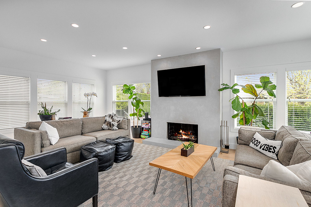 Large contemporary open concept living room in Seattle with white walls, light hardwood floors, a standard fireplace, a wall-mounted tv, beige floor and a concrete fireplace surround.