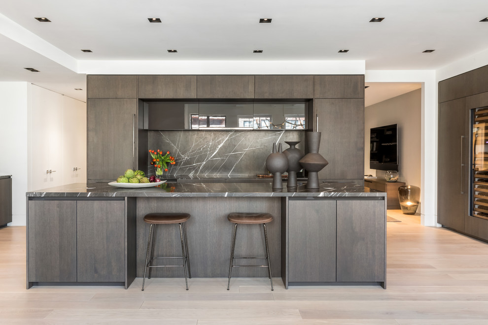 Inspiration for a mid-sized contemporary l-shaped kitchen in New York with dark wood cabinets, panelled appliances, light hardwood floors, with island, flat-panel cabinets, grey splashback, stone slab splashback, beige floor and grey benchtop.