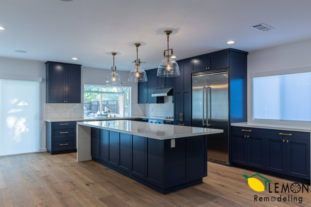 This is an example of a modern kitchen in San Francisco with an undermount sink, blue cabinets, marble benchtops, white splashback, ceramic splashback, stainless steel appliances, light hardwood floors, with island, brown floor and white benchtop.