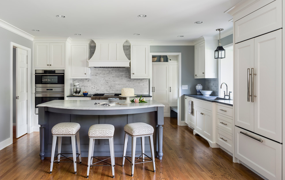 Inspiration for a mid-sized traditional l-shaped eat-in kitchen in Minneapolis with an undermount sink, recessed-panel cabinets, white cabinets, marble benchtops, white splashback, stone tile splashback, panelled appliances, dark hardwood floors and with island.