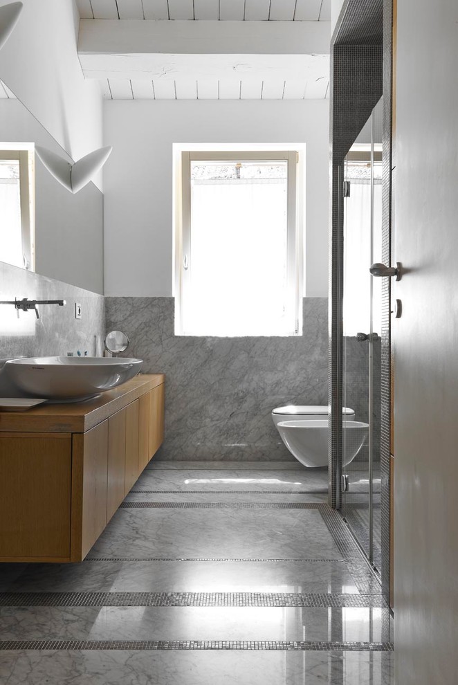 Design ideas for a mid-sized contemporary 3/4 bathroom in Other with flat-panel cabinets, light wood cabinets, a wall-mount toilet, gray tile, stone slab, white walls, marble floors, a vessel sink, wood benchtops, a hinged shower door and brown benchtops.