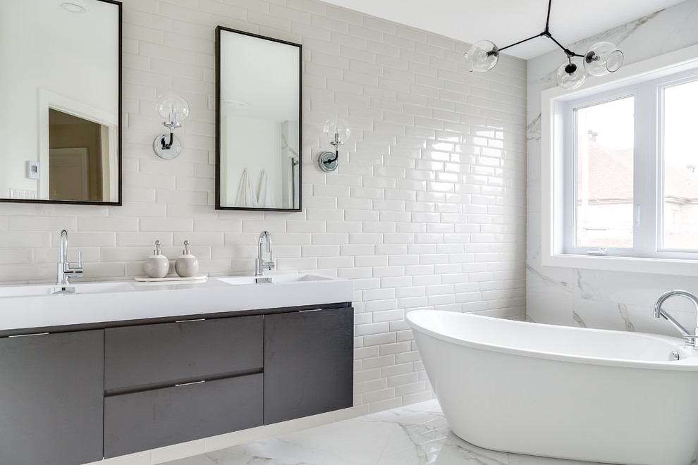 Large contemporary master bathroom in Montreal with flat-panel cabinets, black cabinets, a freestanding tub, a corner shower, a one-piece toilet, white tile, porcelain tile, white walls, porcelain floors, an undermount sink, engineered quartz benchtops, white floor and a sliding shower screen.