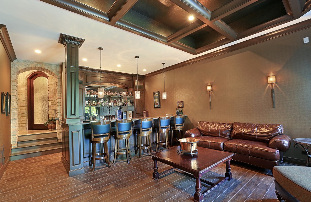 Large traditional galley seated home bar in Chicago with raised-panel cabinets, dark wood cabinets, mirror splashback, medium hardwood floors and brown floor.