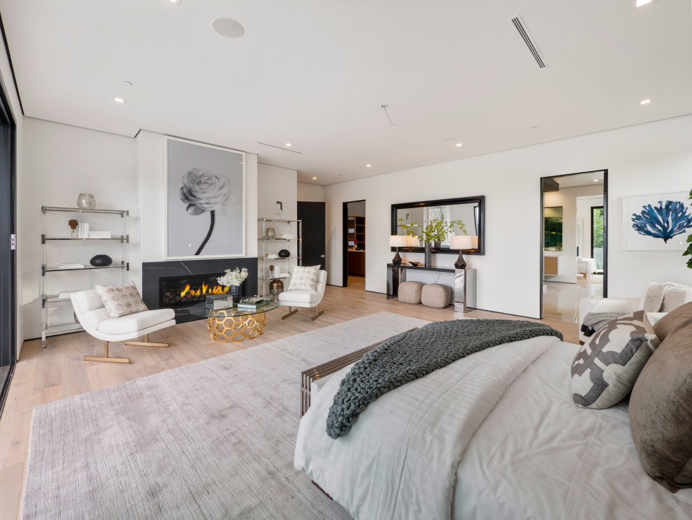 Contemporary bedroom in Los Angeles with white walls, light hardwood floors, a ribbon fireplace, a stone fireplace surround and beige floor.