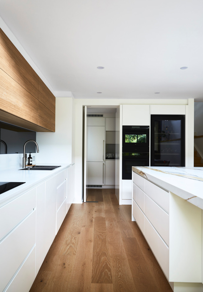 This is an example of a large contemporary l-shaped kitchen pantry in Sydney with a double-bowl sink, flat-panel cabinets, white cabinets, engineered stone countertops, multi-coloured splashback, mirror splashback, black appliances, laminate floors, an island and multicoloured worktops.
