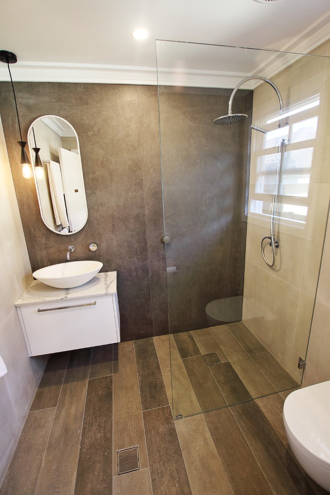 Photo of a mid-sized contemporary bathroom in Sydney with flat-panel cabinets, white cabinets, a corner shower, a wall-mount toilet, brown tile, porcelain tile, brown walls, porcelain floors, a vessel sink, engineered quartz benchtops, brown floor, an open shower and white benchtops.